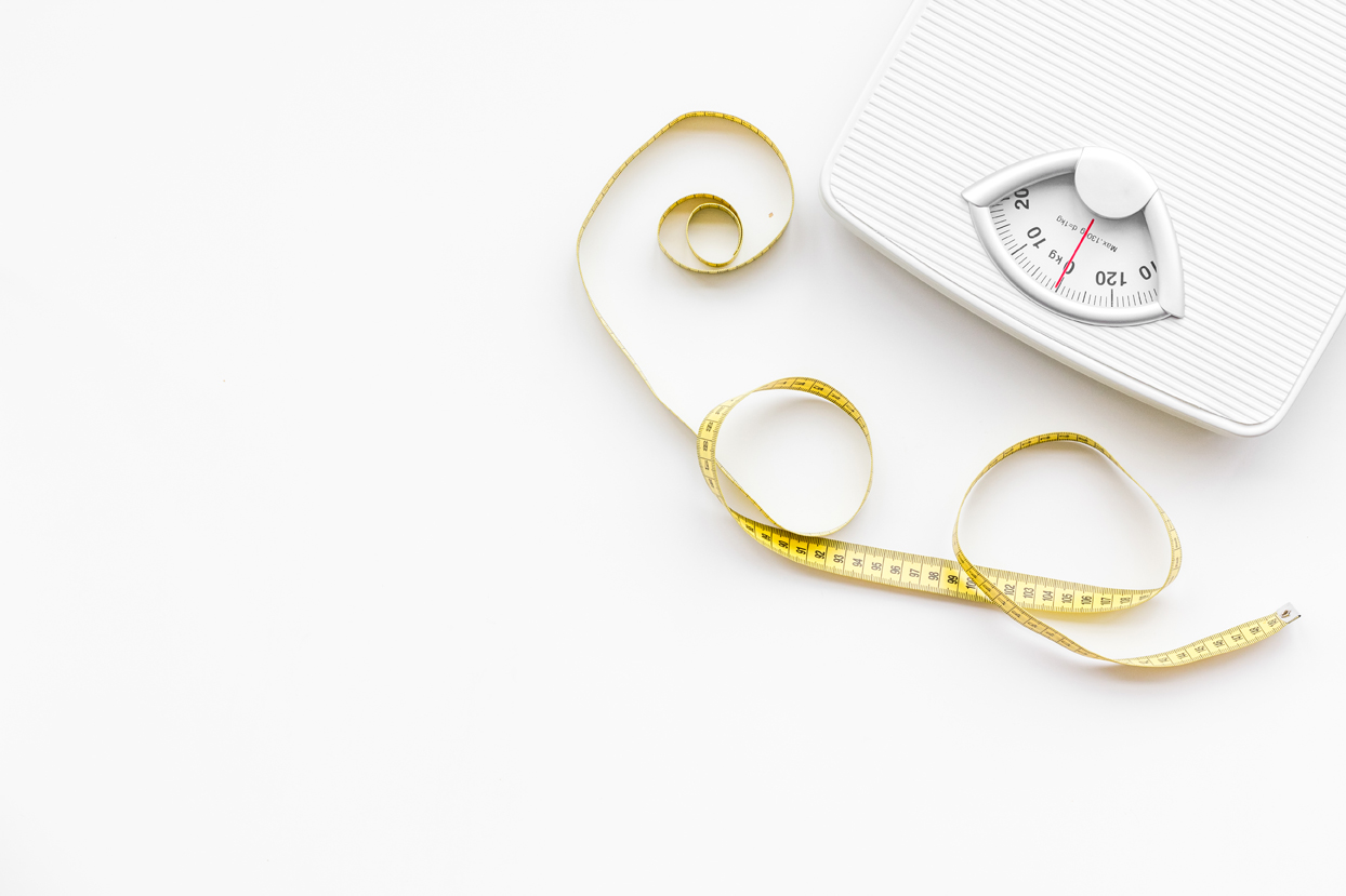 White analog bathroom scale with yellow measuring tape on a white background.